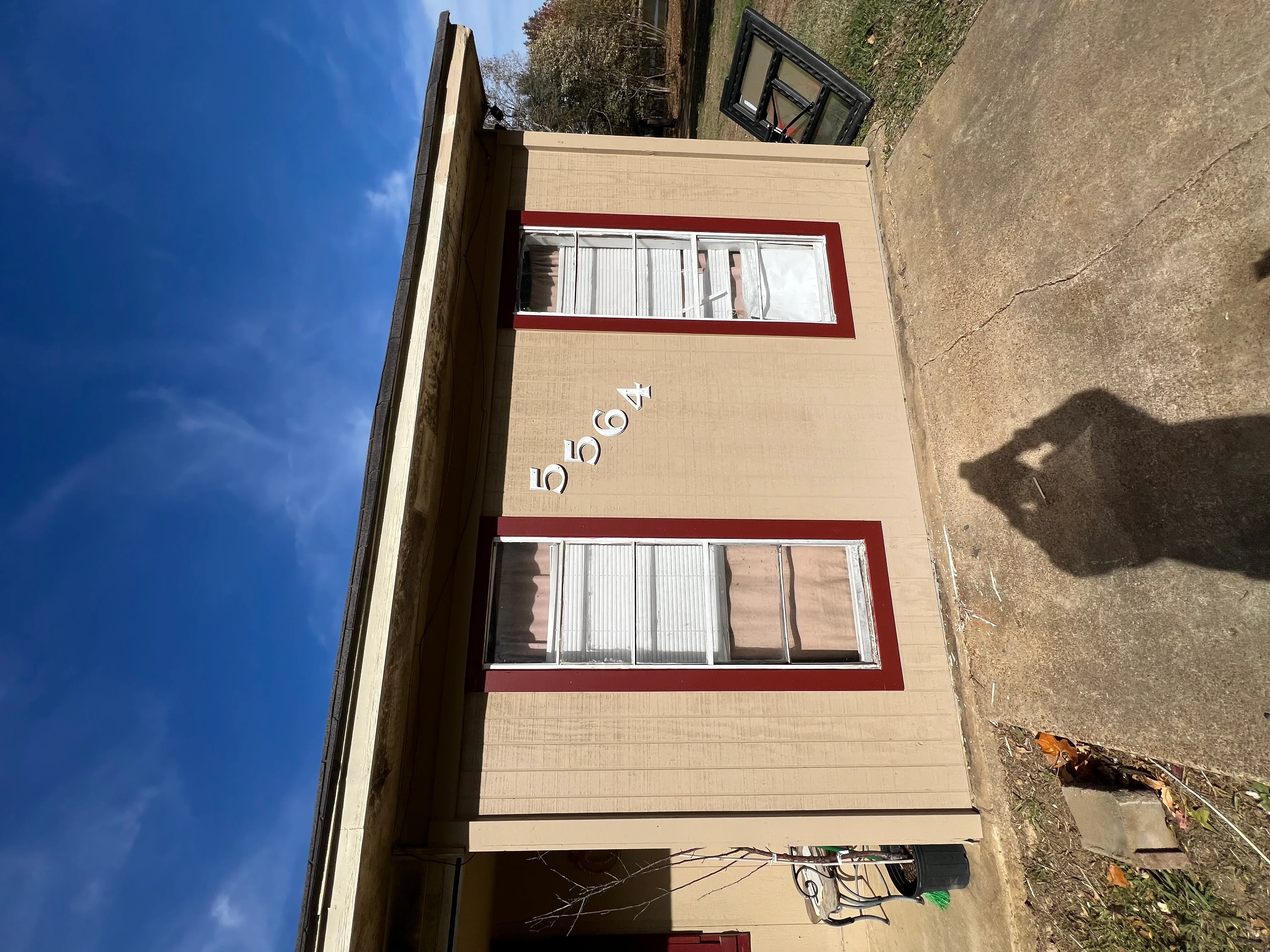 Tan brick residential building with burgundy-trimmed windows and white address numbers