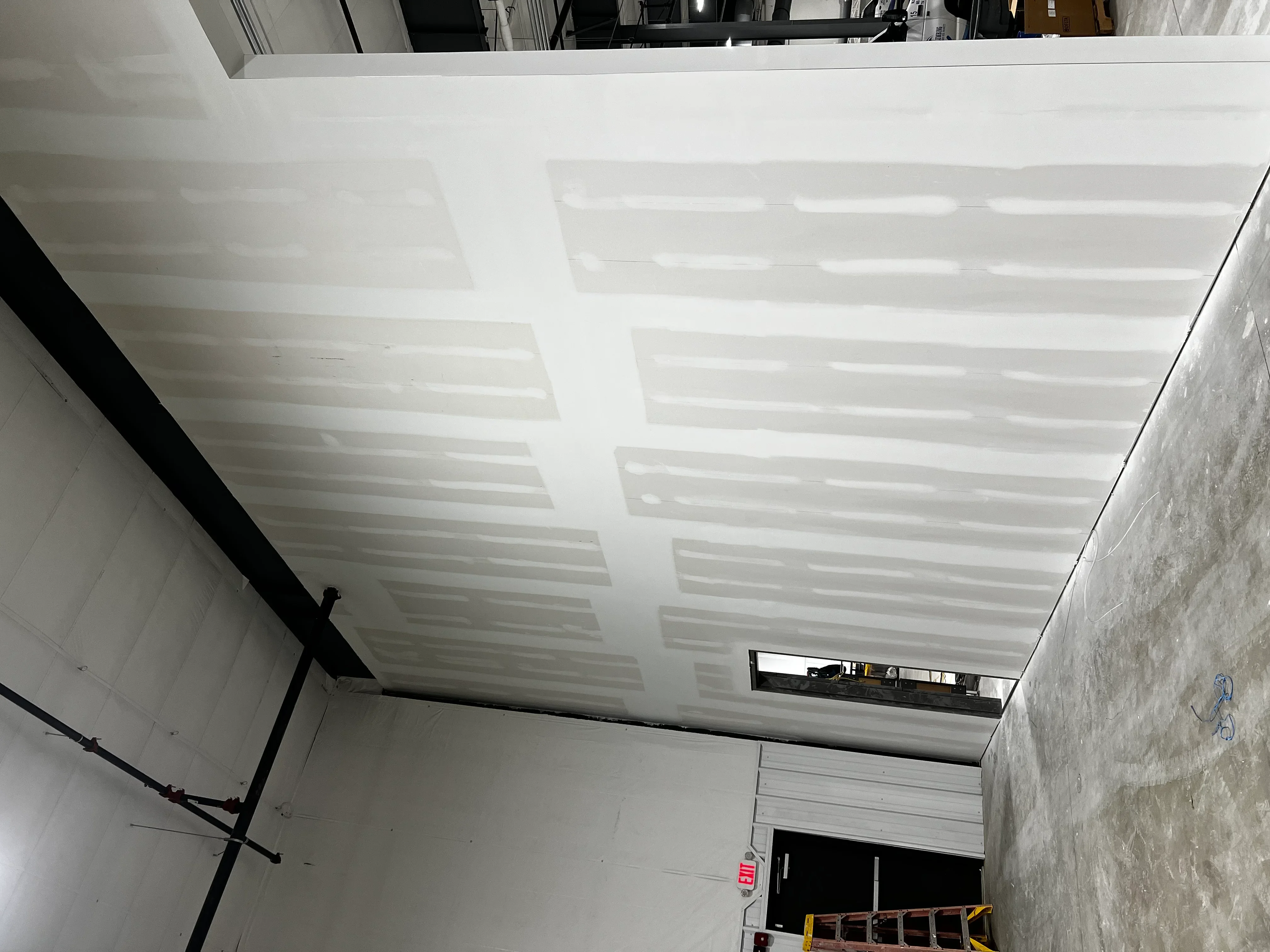 White drywall ceiling with recessed lights and structural beams in commercial interior
