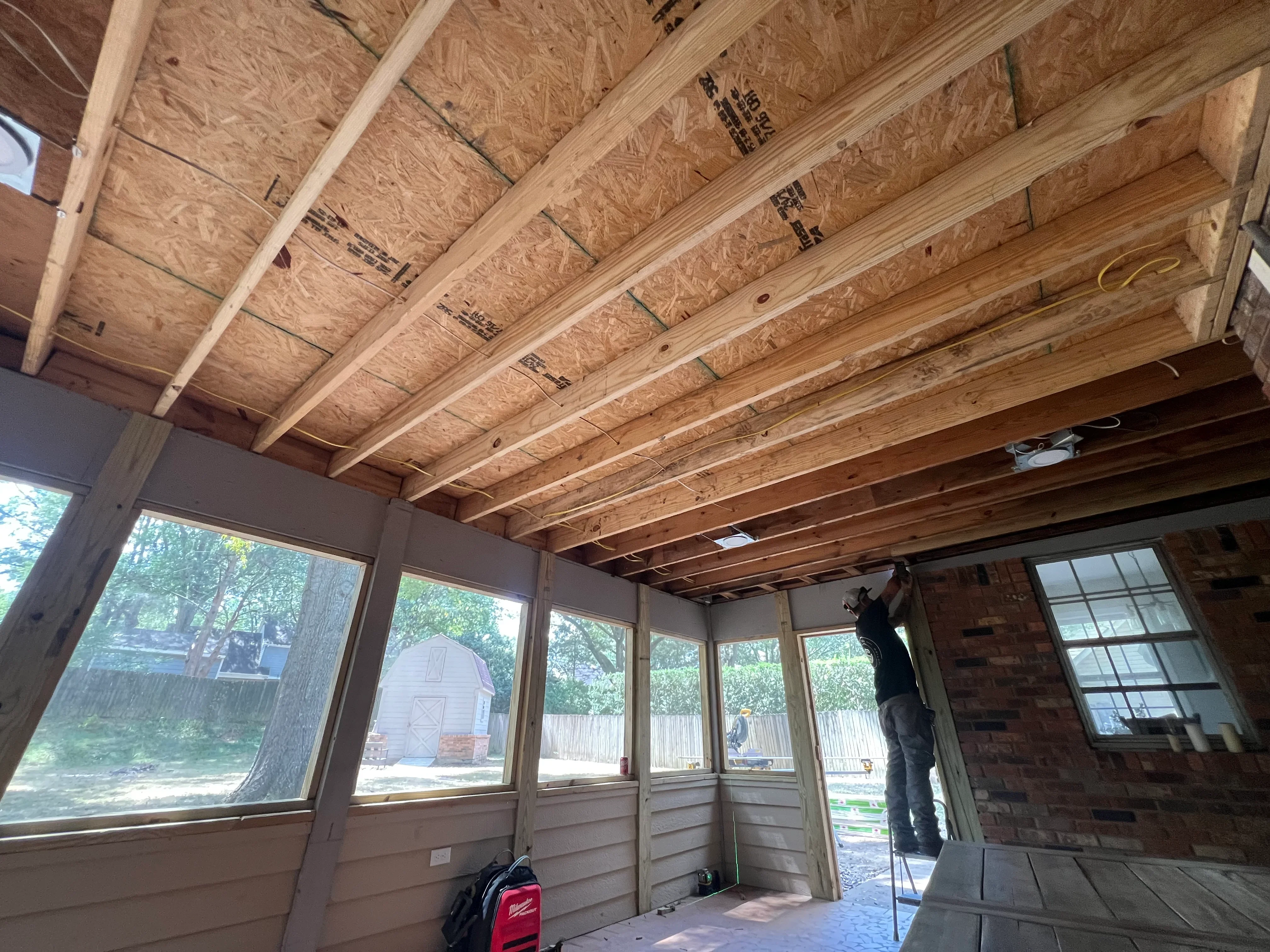 Interior framing of room addition with wooden joists, OSB subfloor, and large windows