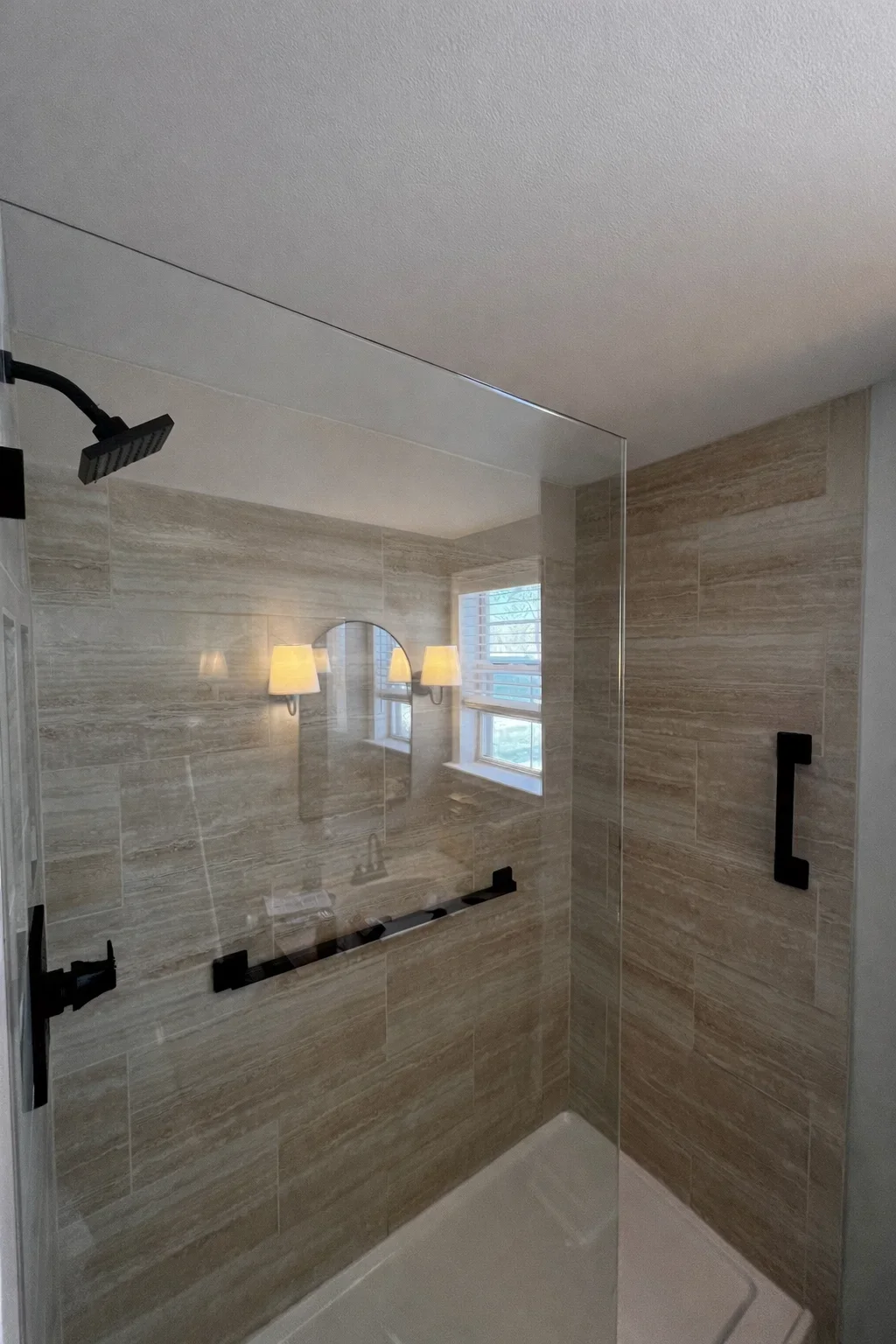 Modern bathroom shower with wood-grain tile, frameless glass doors, and black fixtures