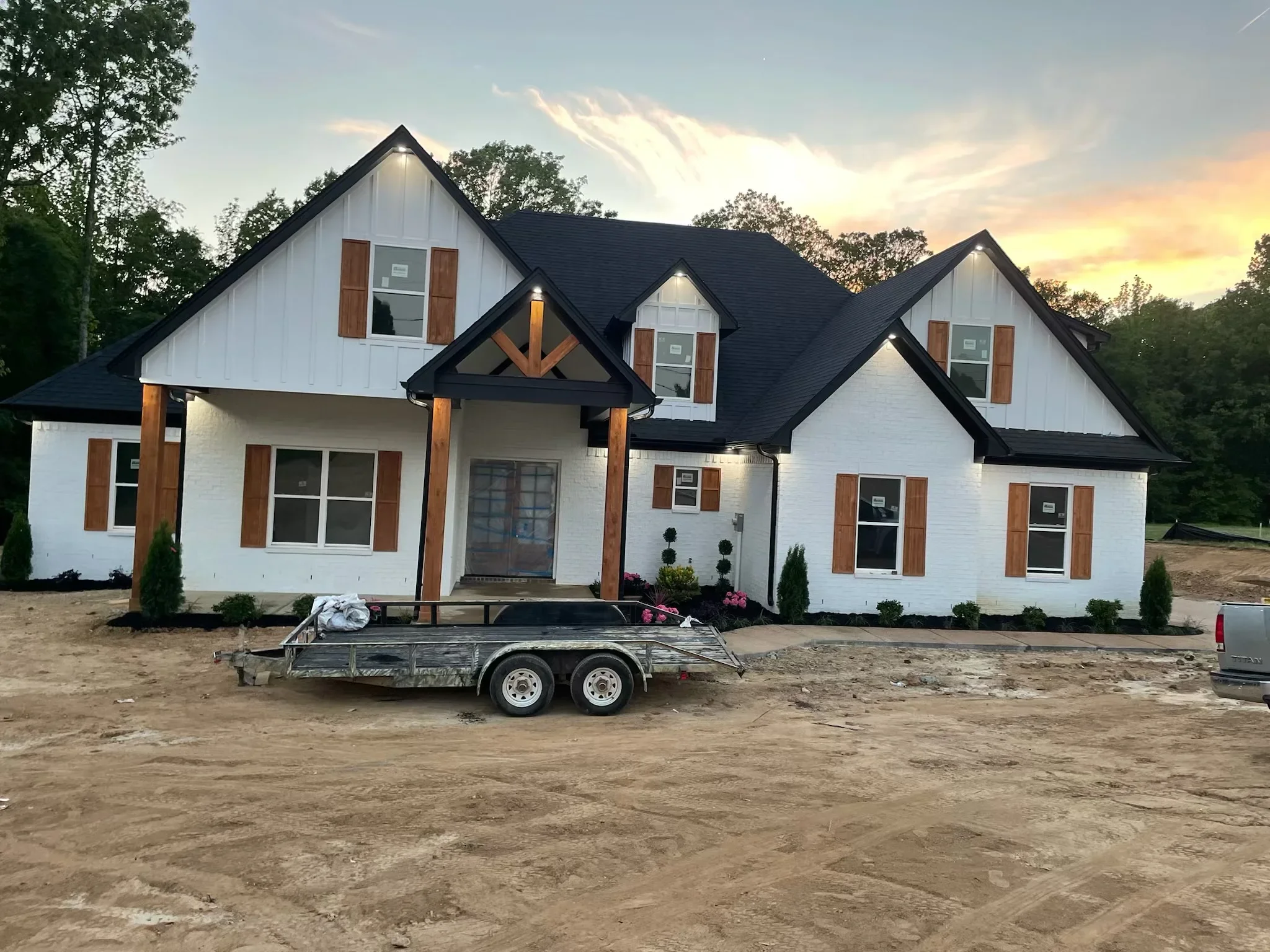 New white brick farmhouse with black roof and wood beams during final construction phase