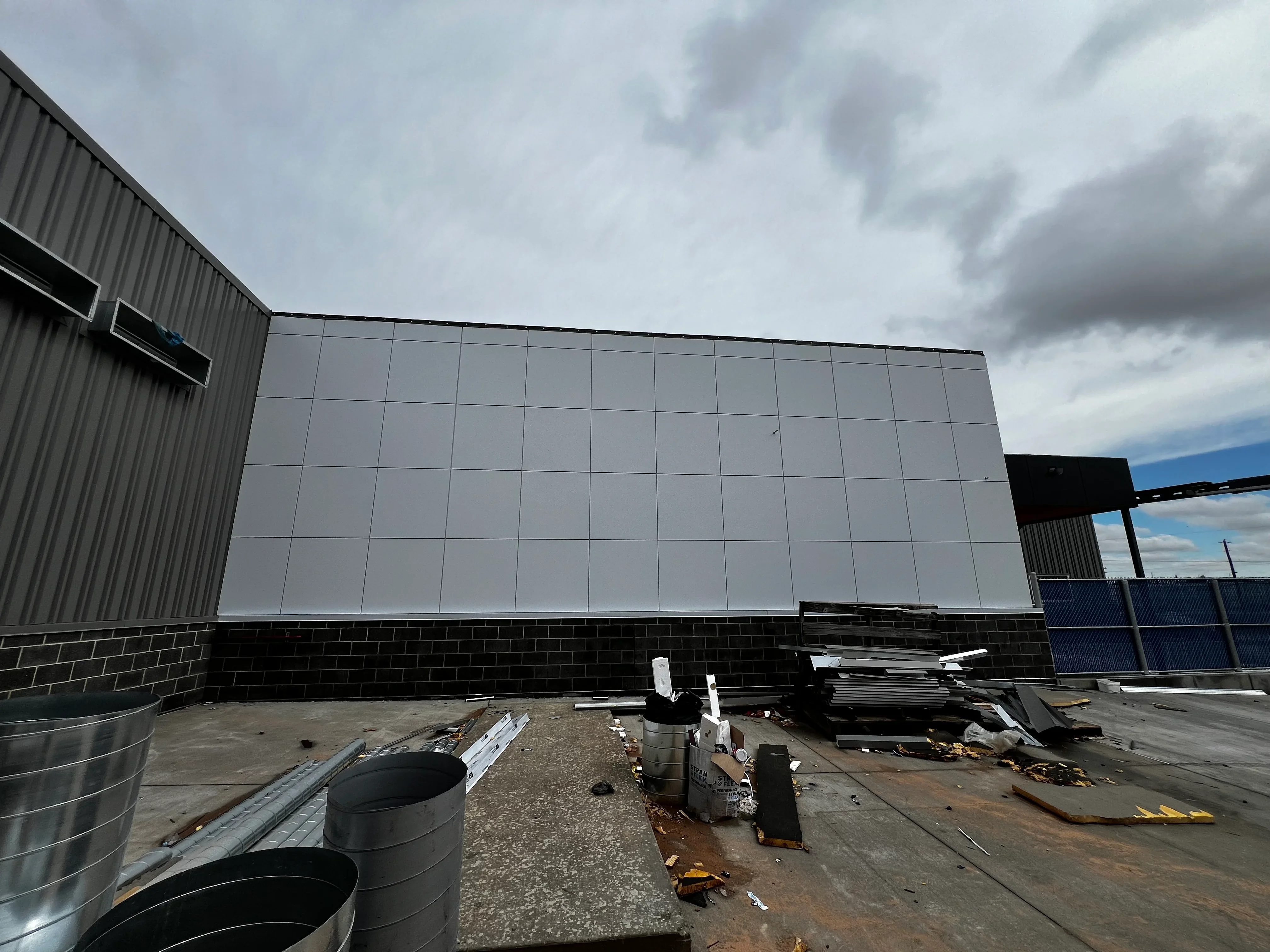 Commercial building with gray metal cladding panels and dark brick base under construction