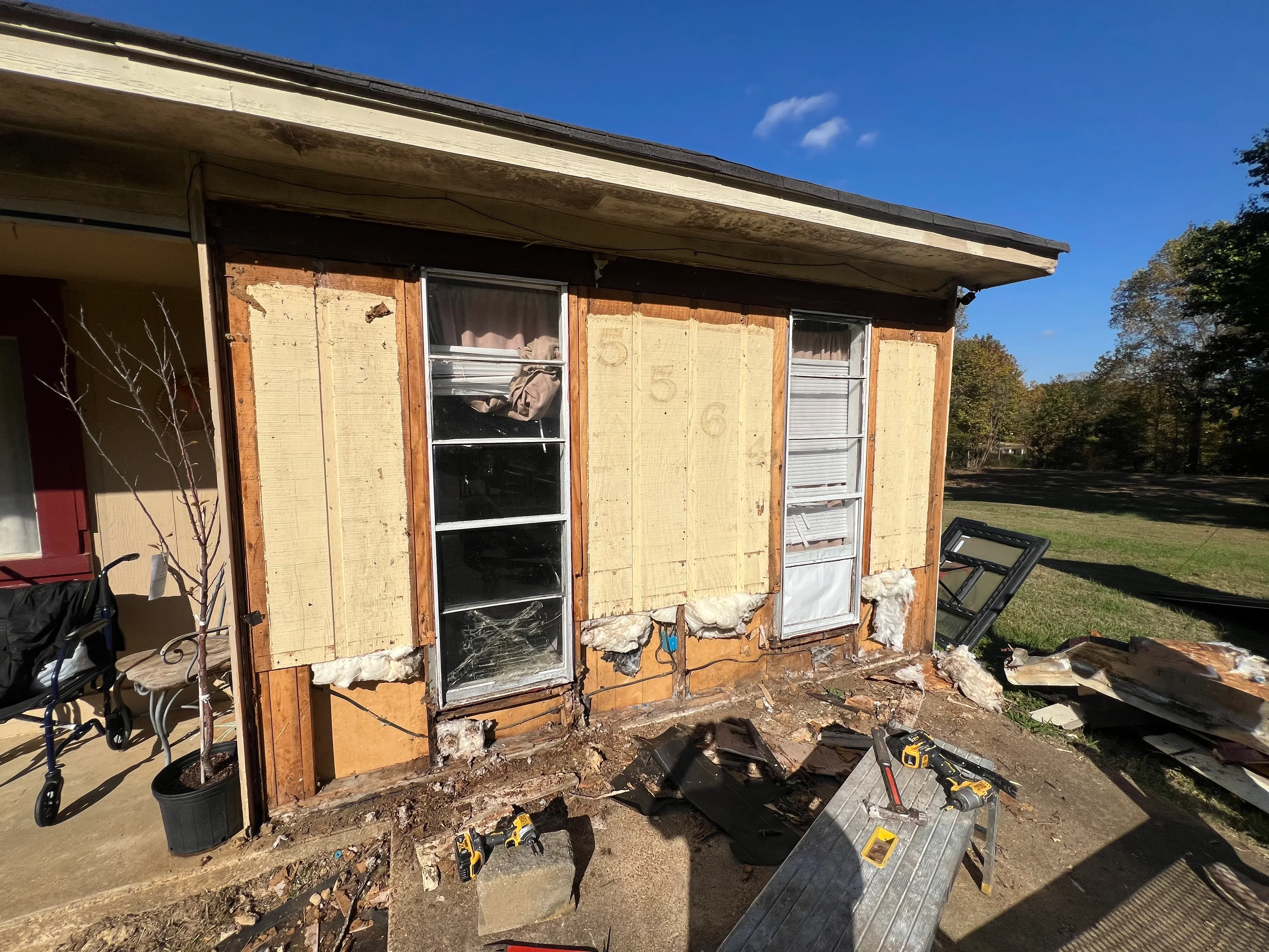 Residential structure undergoing renovation with exposed framing, new windows, and restoration materials on site