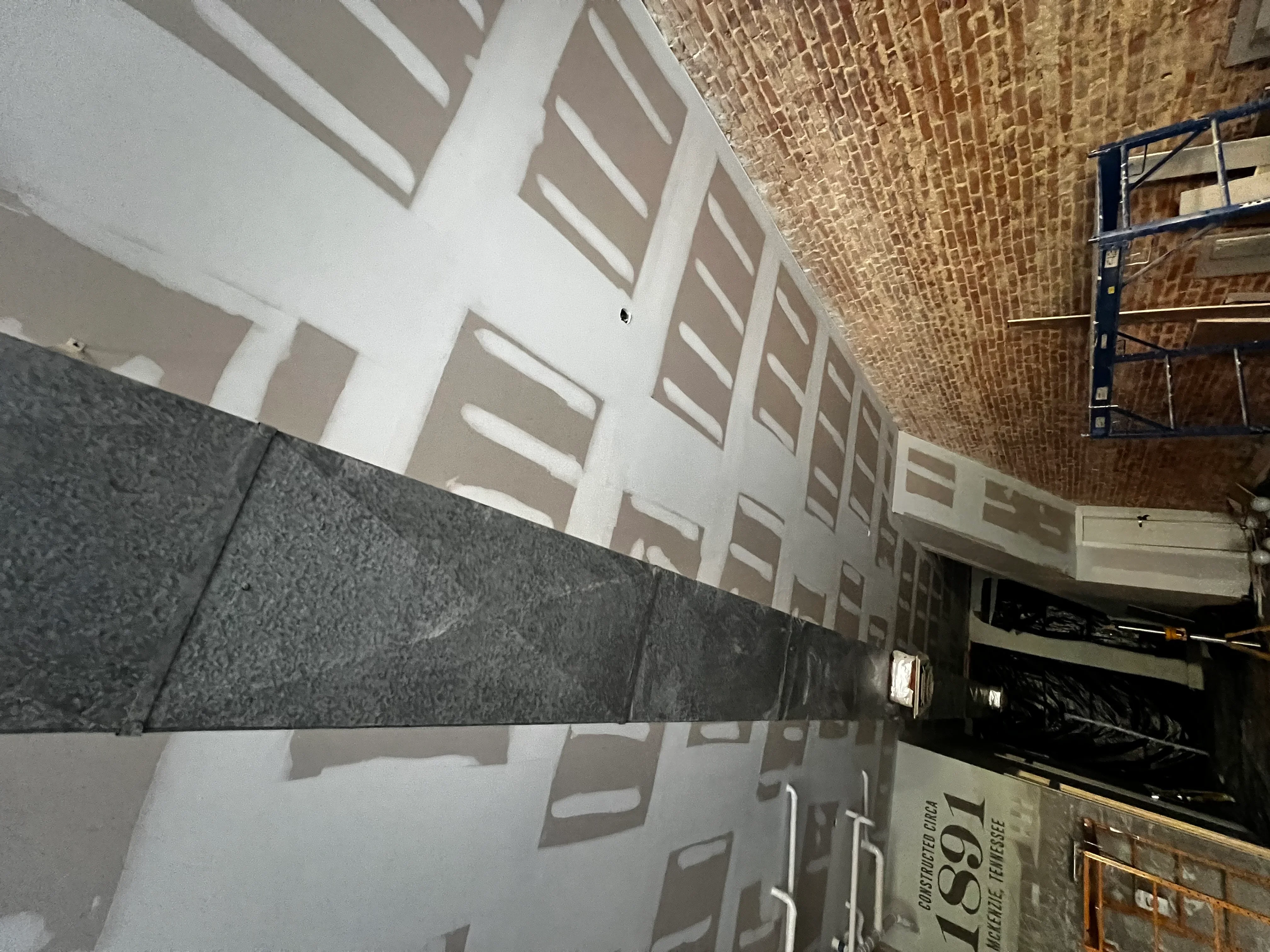 Commercial interior with white drywall walls, exposed brick ceiling, and dark tile wainscoting