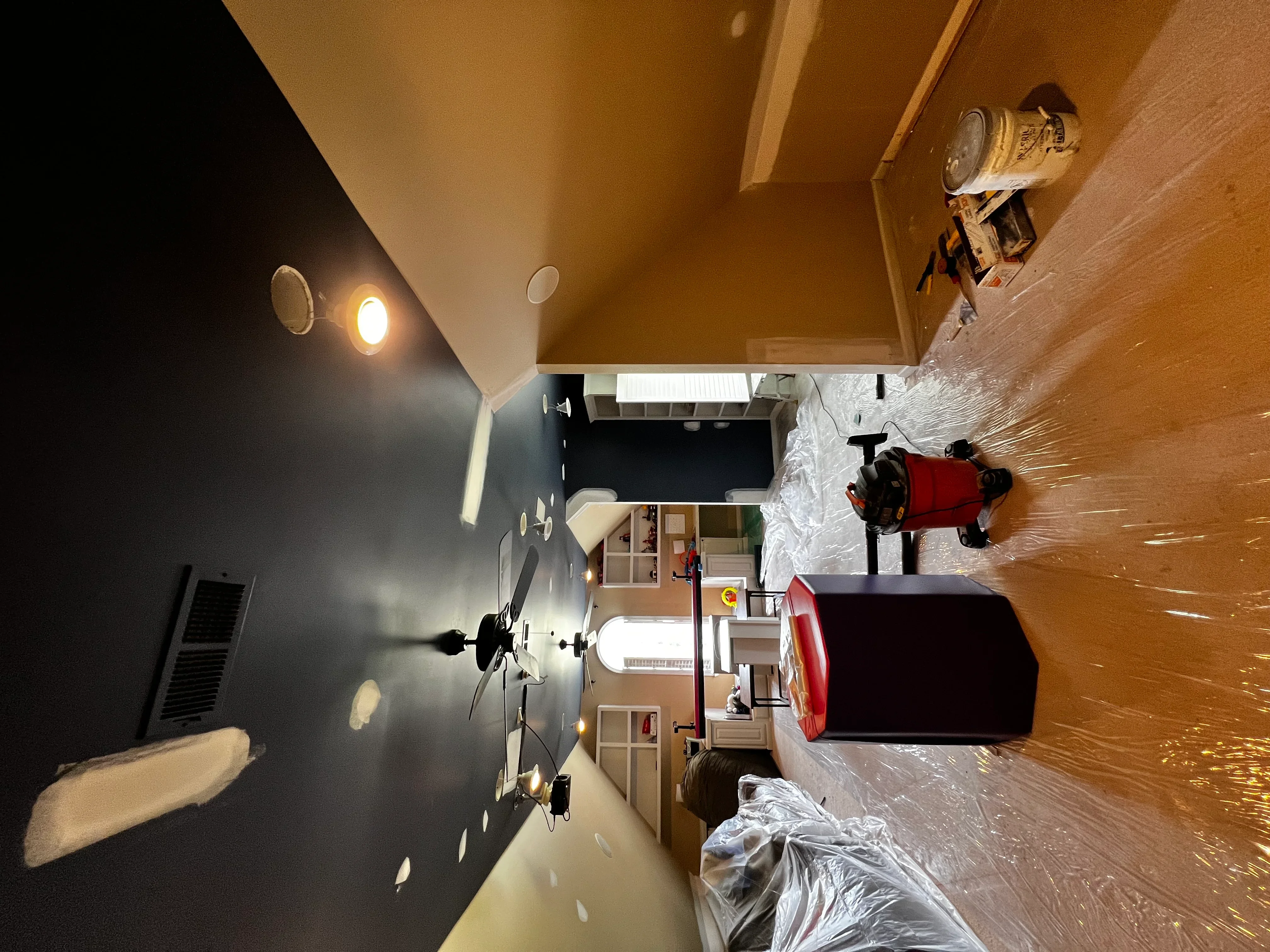 Interior room with newly installed drywall, recessed lighting, and protective floor coverings during construction phase