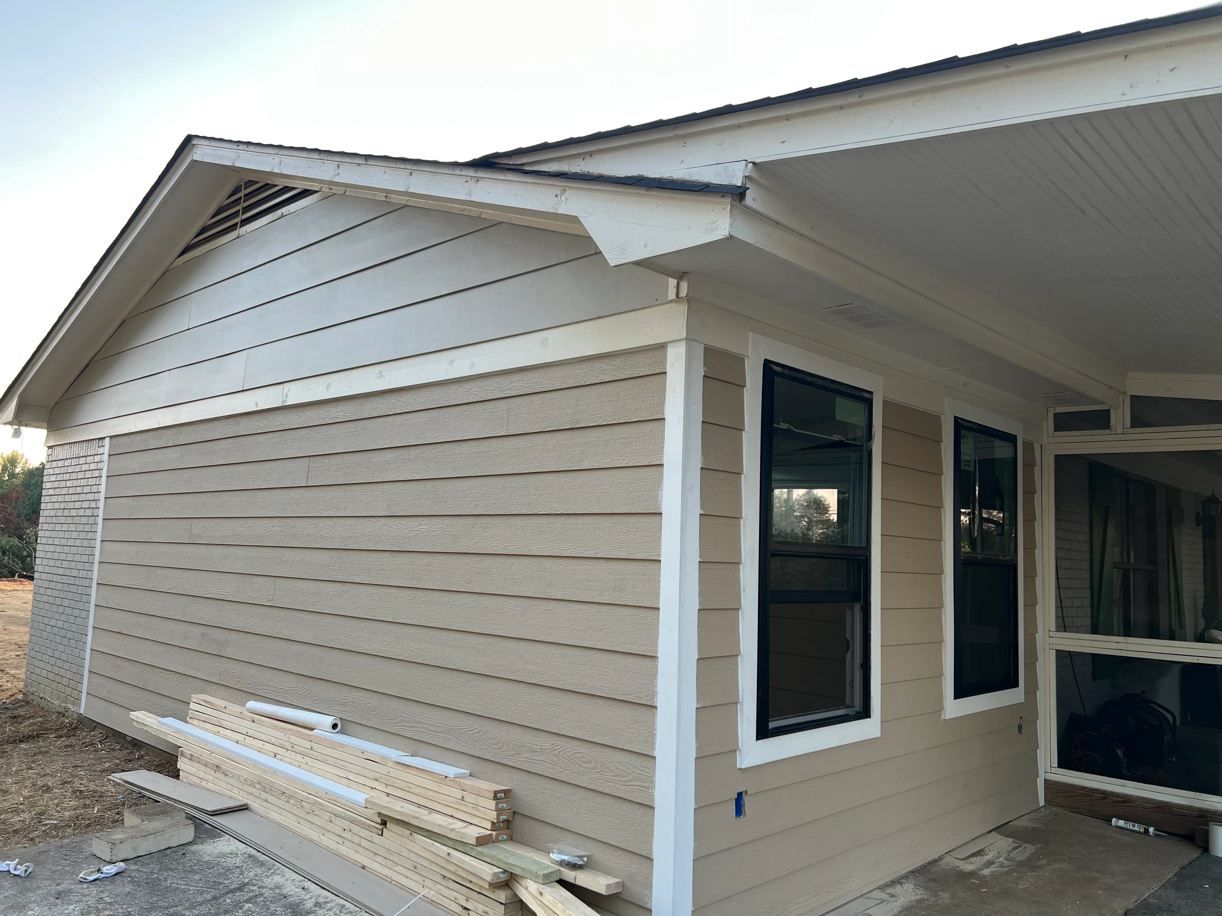 New home addition with tan siding, white trim, and black-framed windows under construction