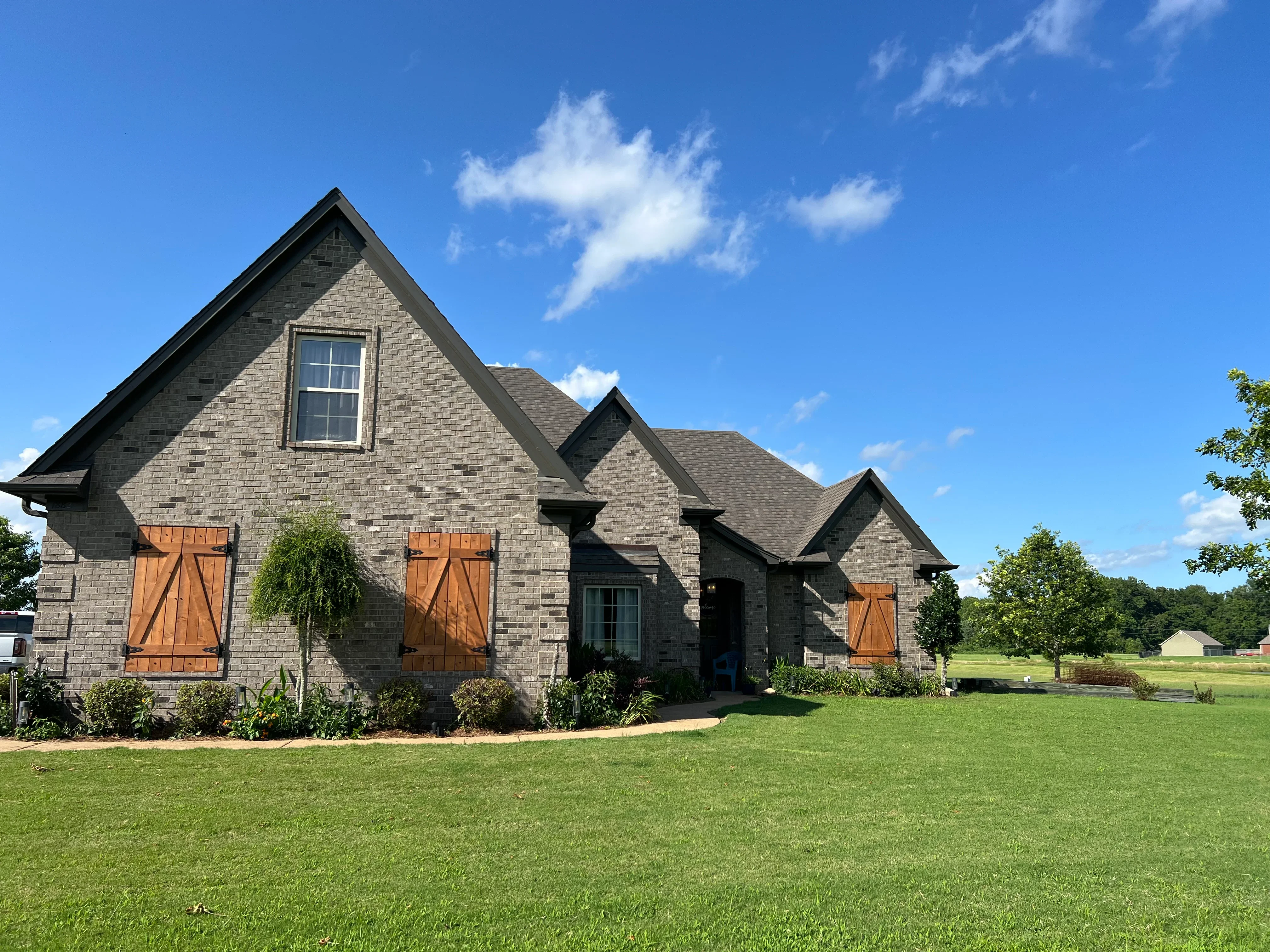 Gray stone residential home with gabled roofs and orange barn doors on manicured lawn