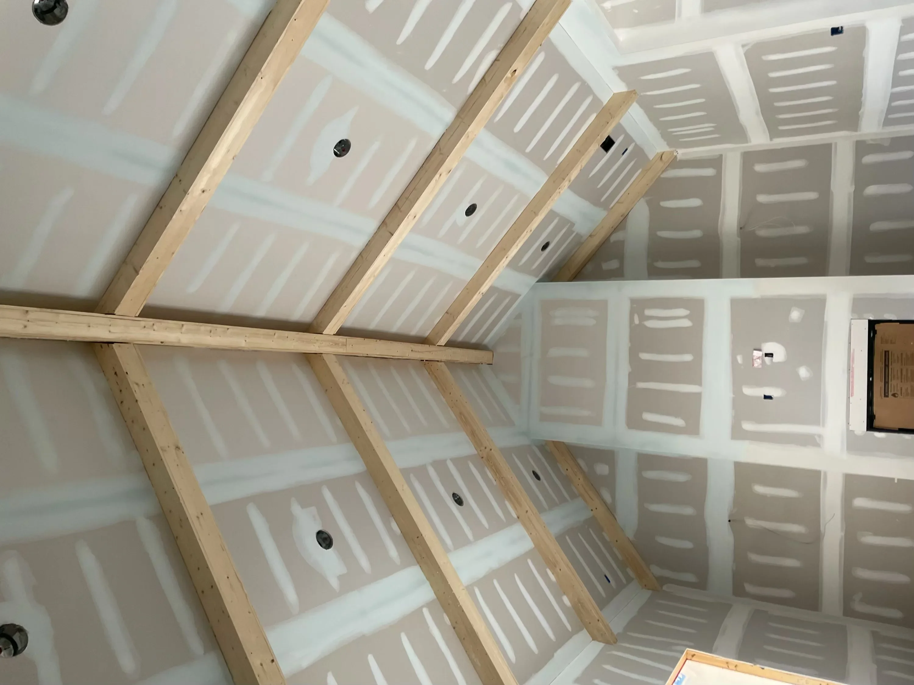Interior drywall installation with wooden framing and electrical rough-ins on angled ceiling